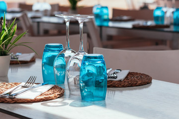 Beach cafe table setup on sunny day outdoor, served for lunch, blue glasses, wicker plates, cutlery. Authentic, simple decor. Beautiful summer holiday concept. Romantic time at resort. Selective focus