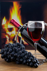 Bottle of wine and glass of wine on the background of the fireplace.