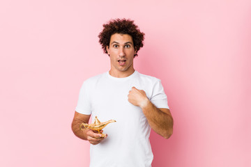 Young caucasian curly man  holding a magic lamp surprised pointing at himself, smiling broadly.