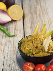 Fresh cooked guacamole on a wooden background. Ingredients for homemade guacamole: avocado, lemon, salt and pepper and tomatoes and tartilla. Close-up.