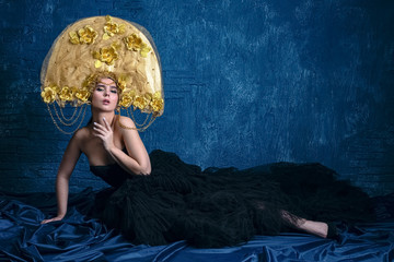 Perfect Woman in dlack Dress and gold hat. Beautiful Fashion Model on Blue Background