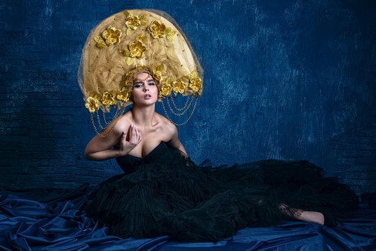 Perfect Woman in dlack Dress and gold hat. Beautiful Fashion Model on Blue Background