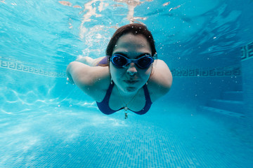 chica joven caucásica nadando en piscina con bañador y gafas. propulsada. 