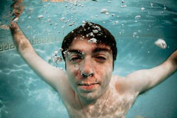 hombre joven caucásico de pelo moreno sumergido en una piscina, sacando burbujas de agua. apnea,...