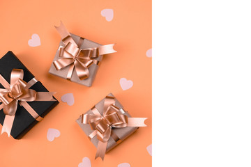 Holiday background. Various handmade gift boxes decorated with pink heart confetti, white frame on orange background. Minimal style and valentines day concept. Flat lay, top view, copy space