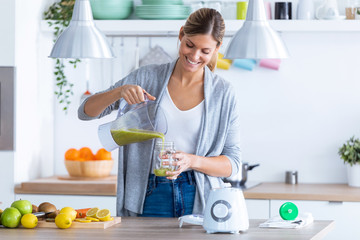 Pretty young woman serving the detox juice she has made in the blender at home.