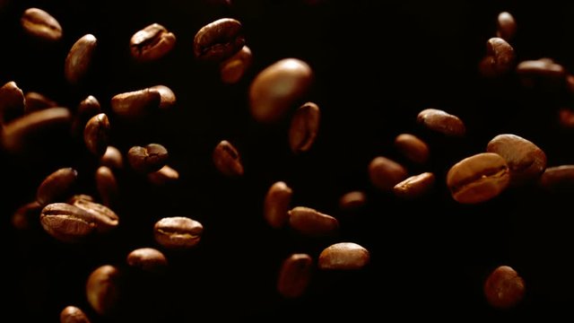 Roasted coffee beans fly and spin on a black background in slow motion