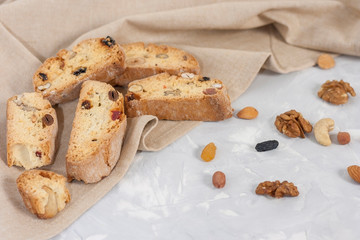 Traditional Italian cookie Biscotti or Cantuccini with hazelnuts, almonds, walnuts on a gray background with a beige linen napkin and slices of dried oranges.