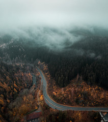 Curvy mountain road in a autumn orange nature landscape with low hanging clouds and dark moody...