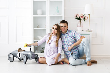 A man and a pregnant woman spend time together, hold apple and sit on the floor. Beautiful bright guest room