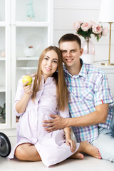 A man and a pregnant woman spend time together, hold apple and sit on the floor. Beautiful bright guest room