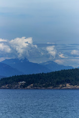 Clouds, coastal mountains, snow, water and greenery viewed from the Thick white clouds drift over the mountain on the Pacific Ocean, BC, Canada