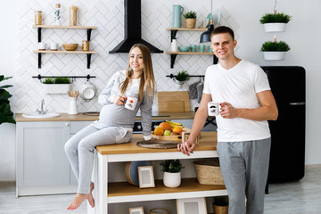 Young couple - man and woman expecting a baby, spend time in the kitchen and drink hot drinks. Awaiting the birth of a baby