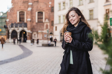 Fototapeta premium Female hand with paper cup of coffee take away. Woman holding cup on the urban background