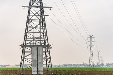 Electricity distribution system. High voltage overhead power line, power pylon, steel lattice tower standing in the field. Blue sky as a background.