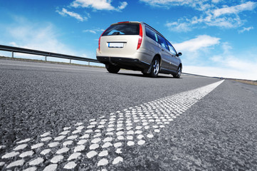 A silver car on the countryside road against sky with clouds