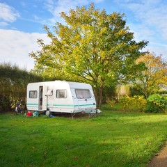 Caravan trailer on a green lawn under the trees in camping, on a sunny Autumn day in France