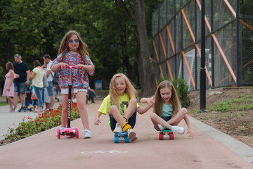 little cute girls with sunglasses and cap sitting on a skateboard. photo of cute preteen girl with skateboard outdoors.