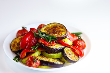  Grilled vegetables on a white plate. Peppers, tomatoes, zucchini, eggplant, rosemary and herbs are nicely served on a plate. Baked red bell pepper with eggplant. Restaurant serving vegetables