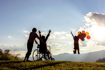 Happy family on the mountain,woman is on a wheelchair looking little girl jumping playing with air...
