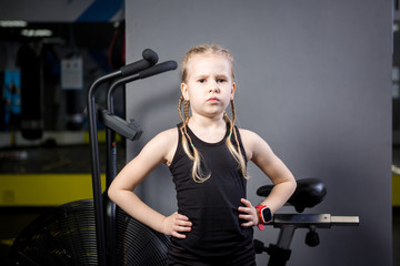 Small attractive caucasian child using exercise bike in the gym. Fitness. A little athlete using an...