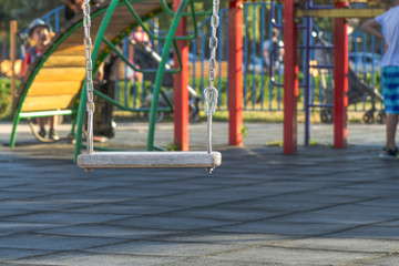 Fototapeta na wymiar empty swing at the playground. The concept of childhood and fun. wooden plaque on a metal chain