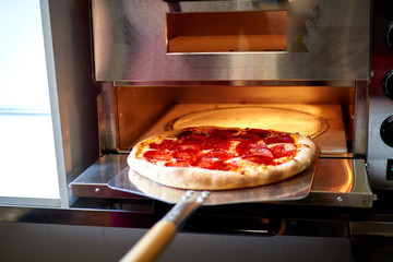 baker puts pizza in the oven