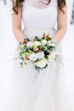 Wedding bouquet with flowers and cotton in hands of the bride. Winter time, snowy forest. Cropped image
