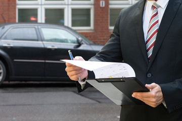 Man Standing In Front Of Car Holding Clipboard
