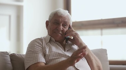 Happy senior man holding cellphone talking on phone at home - Powered by Adobe