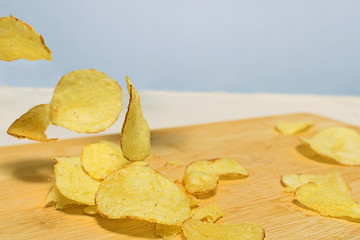 Natural potato chips fall on a wooden cutting board lying on the table. Close to copy space.
