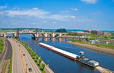 Near Shepard Road along the Mississippi River a large barge with its cargo cruises to the Lift Bridge and the Robert Street Bridge in downtown St. Paul, Minnesota.