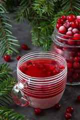 Frozen cranberry berry in a jar and cranberry juice in a glass on the table decorated with branches of the Christmas tree. Christmas winter time