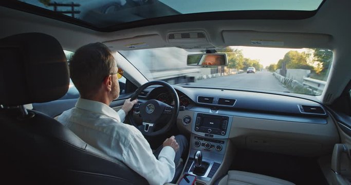 Back view of stylish businessman in stylish sunglasses driving car across the city. Male driver drives automobile. Navigation. Business people lifestyle. Traveling by auto. Office manager director.