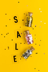 Sale in black letters on a yellow background with confetti. Flat lay style. Concept specially offer. Three small glass bottles with confetti