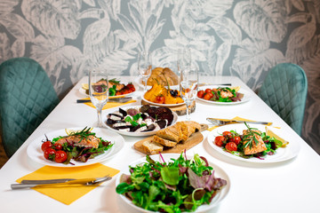 Salmon steak with arugula and vegetables. A feast with people. Beautiful canned white table with food. Festive dinner. Family at the table. Food for lunch
