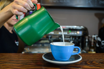 Pouring milk into fresh and aromatic coffee in a cozy coffee shop