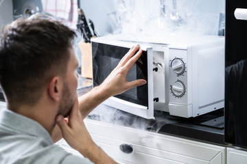 Man Looking At Fire Coming From Microwave Oven