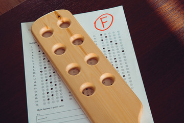 Bad school report card. "F" mark in test. Domestic spanking and corporal punishment concept. Wooden paddle for spanking.