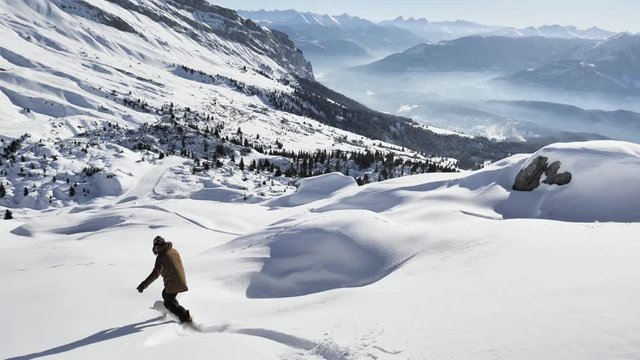 A girl is snowboarding in the backcountry during the winter in Swiss Alps. Shot in 4k with a gimbal.