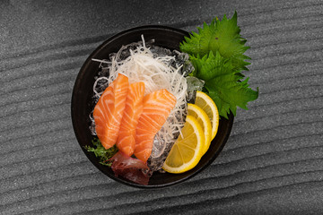 Sashimi with Tuna with slice of lemon fresh greens on bamboo leaf and in plate full of ice.
