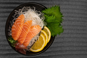 Sashimi with Tuna with slice of lemon fresh greens on bamboo leaf and in plate full of ice.