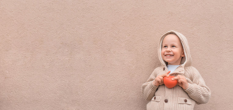 Little boy, autumn beige wall, toy heart, help support concept, gift donation love mother valentines day, happy smiling, free space copy text. Christmas happiness fun relaxation. Holiday concept.