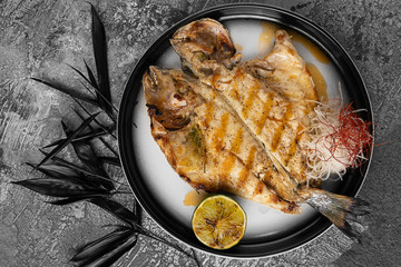 Baked fish with lemon and herbs. Dorado on a plate with vegetables.
