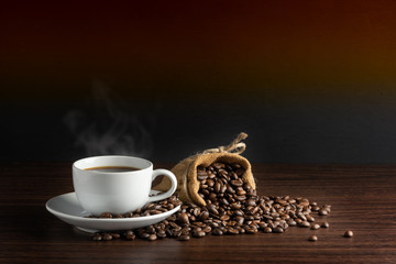 white cup of hot coffee with smoke with coffee beans and sackcloth full of coffee beans with rope