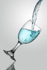 pouring water on tlted champange glass on white background