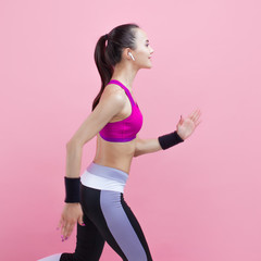 A young attractive girl runs with smile, wireless headphones and in a bright sports top, on a pink background, cardio.