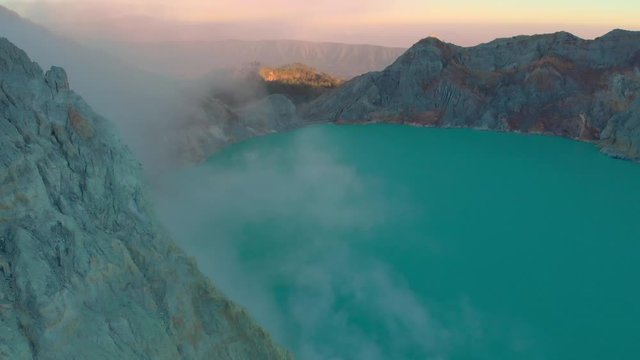 Aerial shot. Sunrise at a famous active Ijen volcano or Kawah Ijen on the Java island. Its crater is filled with the biggest in the world acid lake. And there is a sulfur mine where volcanic gasses go