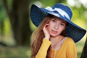 Jolie jeune femme portant un chapeau estival bleu assise sous un arbre
