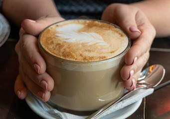 Big cappucino cup with coffee art on a foam with woman hands
